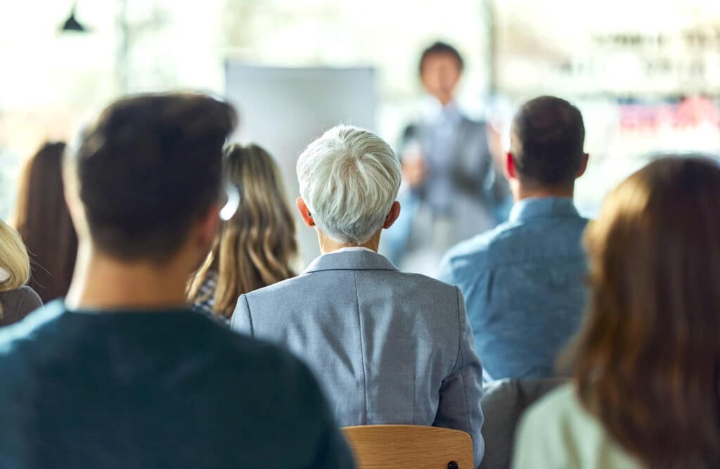 Back view of group of workers in a board room. Focus is on woman in the middle