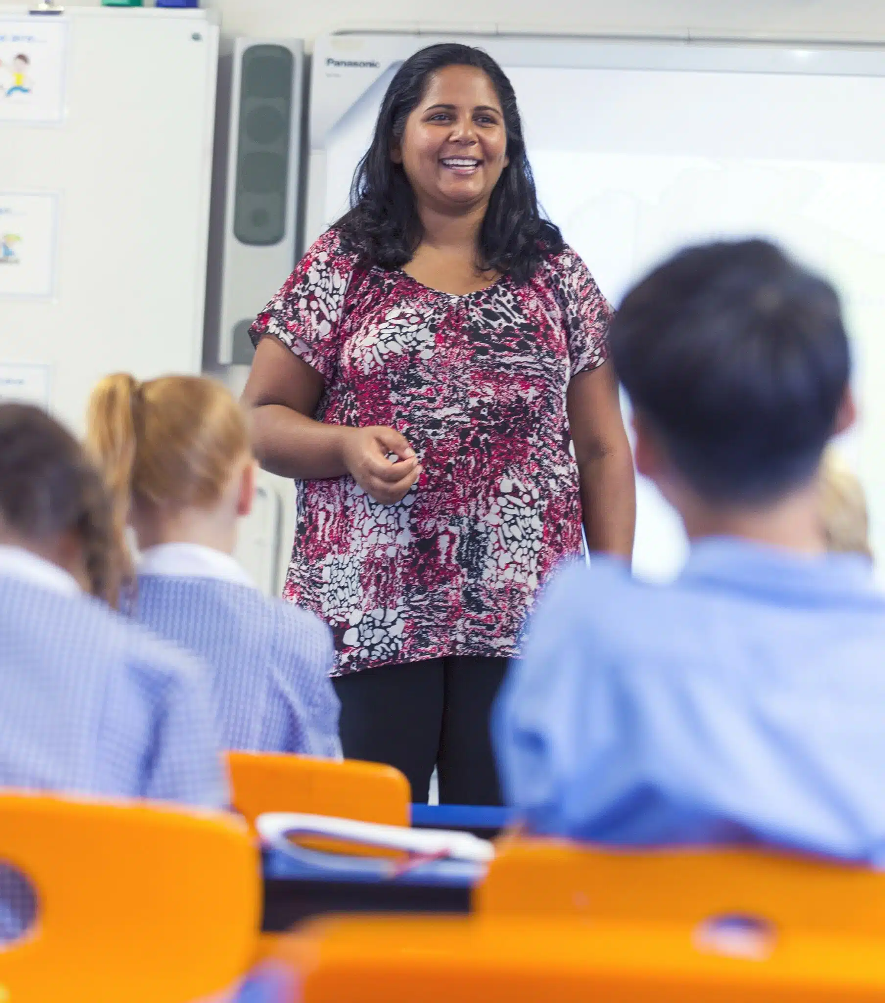 Aboriginal Elementary school teacher with the class. She is happy and smiling. The students are wearing uniforms in the classroom.