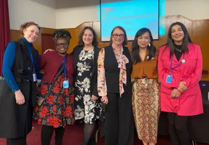 DCA's delegation to CSW68 stand with other delegates in front of a stage at CSW68