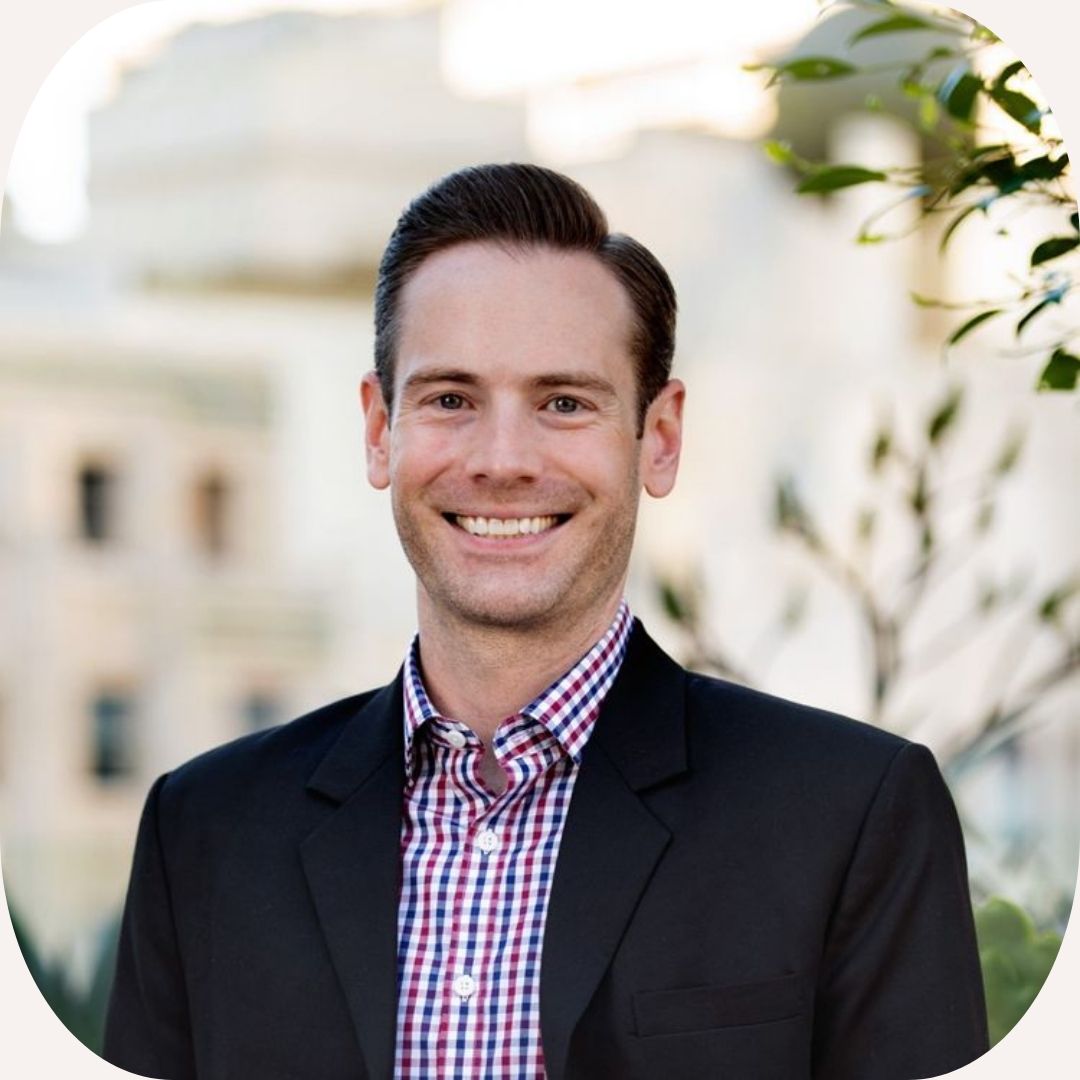 Headshot of Ian Goshko who has short, brown hair and wears a purple shirt and dark jacket.