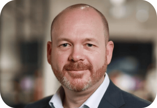 Headshot of Chris Lamb, a white man with a bald head and red beard wearing a dark grey blazer and a white button-up shirt.