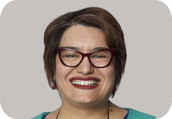 Headshot of Elizabeth Hristoforidis, a woman with short brown hair, olive skin, dark red lipstick and dark funky glasses. She wears a necklace and a green top.