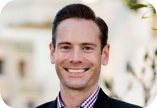 Headshot of Ian Goshko, a young, white man who has short, brown hair and wears a purple shirt and dark jacket.
