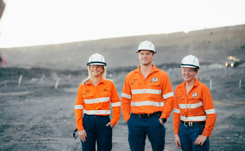 Three workers, two women and one man, in hard hats and high visibility clothing stand out in a field.