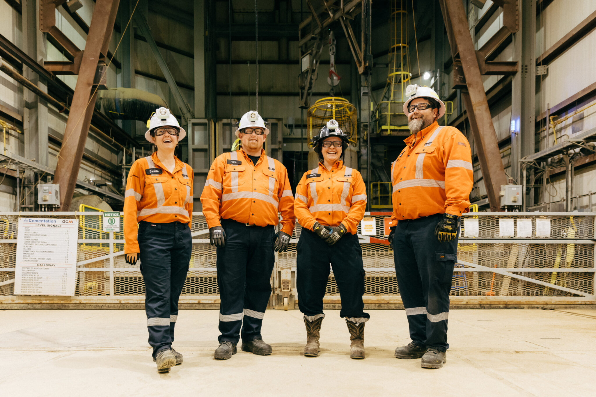 Two women and two men in hard hats and high-visibility clothing stand in an industrial building in front of machinery.