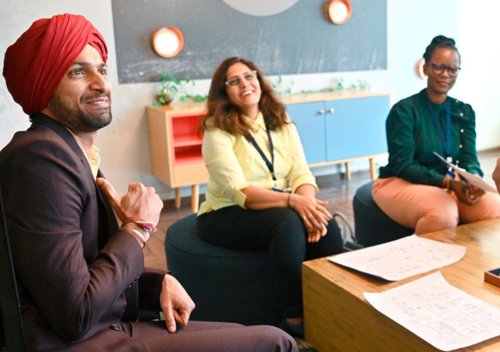 Three workers sit in a workplace setting, smiling at an unseen person.