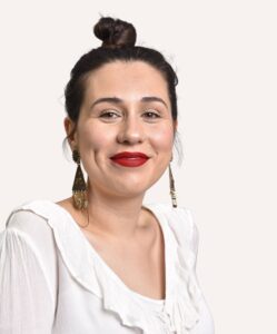 Headshot of Dr Rose D'Almada-Remedios wearing a white shirt, bronze earrings and red lipstick 