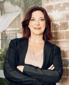 Catherine Fitzpatrick's headshot: a woman with shoulder length auburn hair and blue eyes, wearing a pink blouse and navy blazer. 