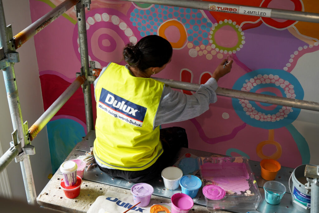 A woman wearing a Dulux high-visibility vest painting a mural.