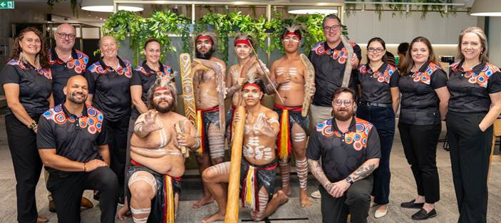 WorkCover employees pictured standing with the Nunukul Yuggera Aboriginal Dance Company at WorkCover’s Innovate Reconciliation Plan launch event, May 2026